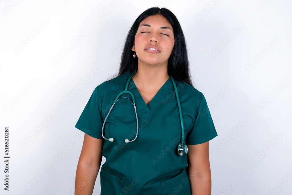 Doctor hispanic woman wearing surgeon uniform over white wall looking sleepy and tired, exhausted for fatigue and hangover, lazy eyes in the morning. Doctor hispanic woman wearing surgeon uniform over white wall looking sleepy and tired, exhausted for fatigue and hangover, lazy eyes in the morning.