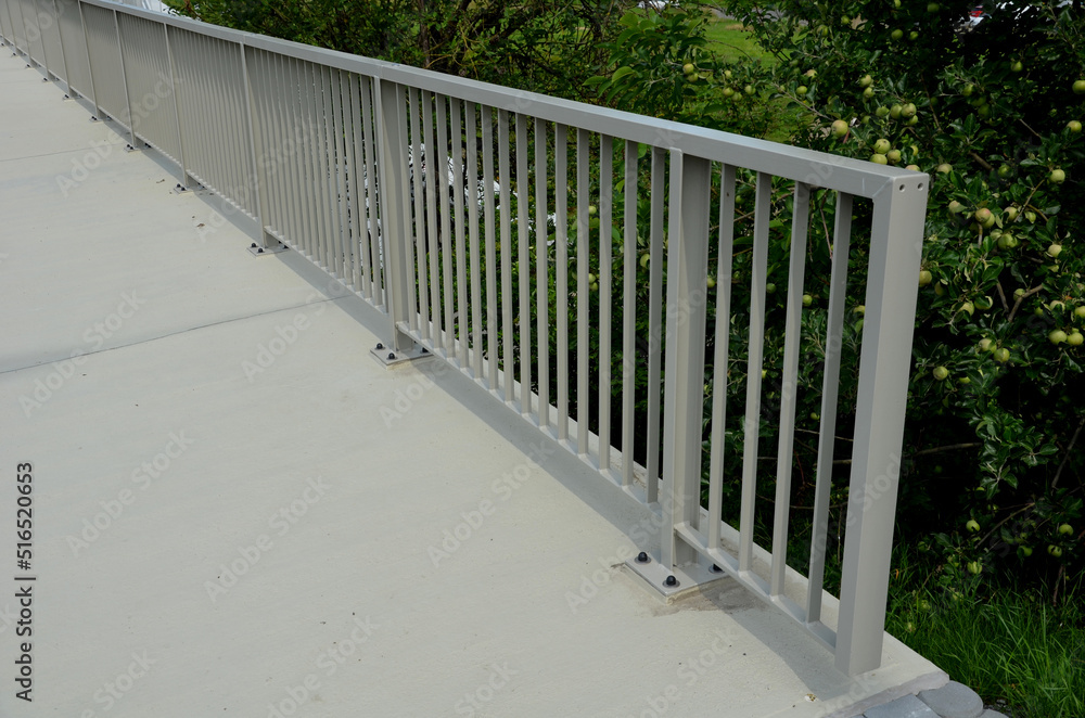 railing at the bridge with vertical fence bars anchored to the ground with four concrete screws. plastic caps