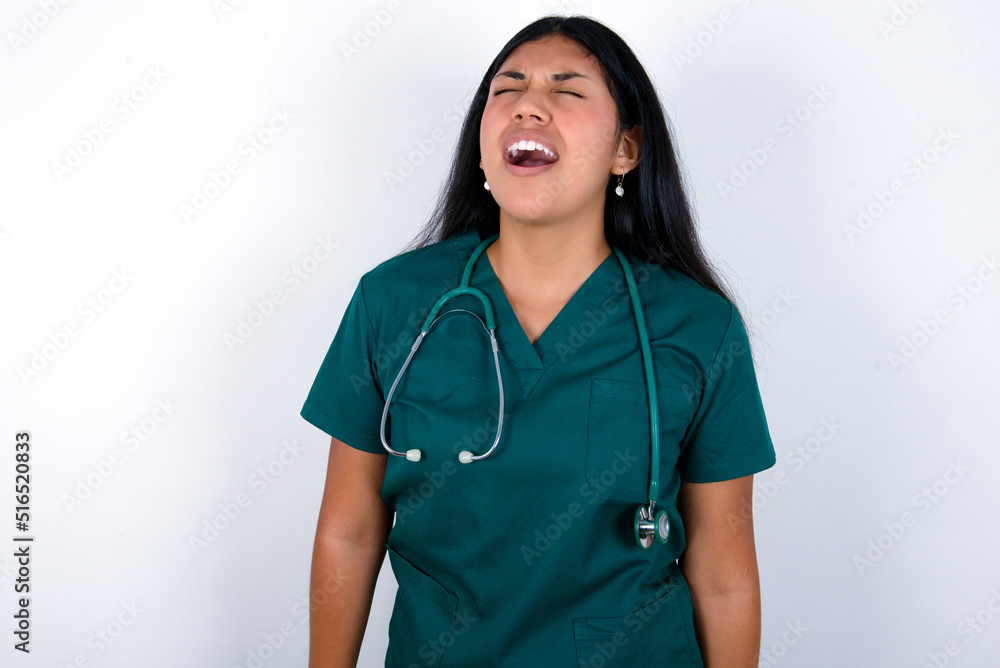 Doctor hispanic woman wearing surgeon uniform over white wall angry and mad screaming frustrated and furious, shouting with anger. Rage and aggressive concept. Doctor hispanic woman wearing surgeon uniform over white wall angry and mad screaming frustrated and furious, shouting with anger. Rage and aggressive concept.