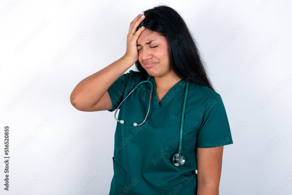 A very upset and lonely Doctor hispanic woman wearing surgeon uniform over white wall crying,