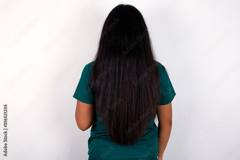 The back view of a Doctor hispanic woman wearing surgeon uniform over white wall. Studio Shoot. The back view of a Doctor hispanic woman wearing surgeon uniform over white wall. Studio Shoot.