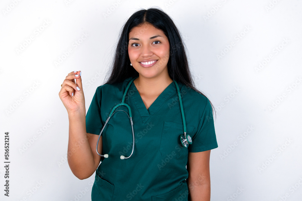 Doctor hispanic woman wearing surgeon uniform over white wall pointing up with hand showing up seven fingers gesture in Chinese sign language QÄ«. Doctor hispanic woman wearing surgeon uniform over white wall pointing up with hand showing up seven fingers gesture in Chinese sign language QÄ«.