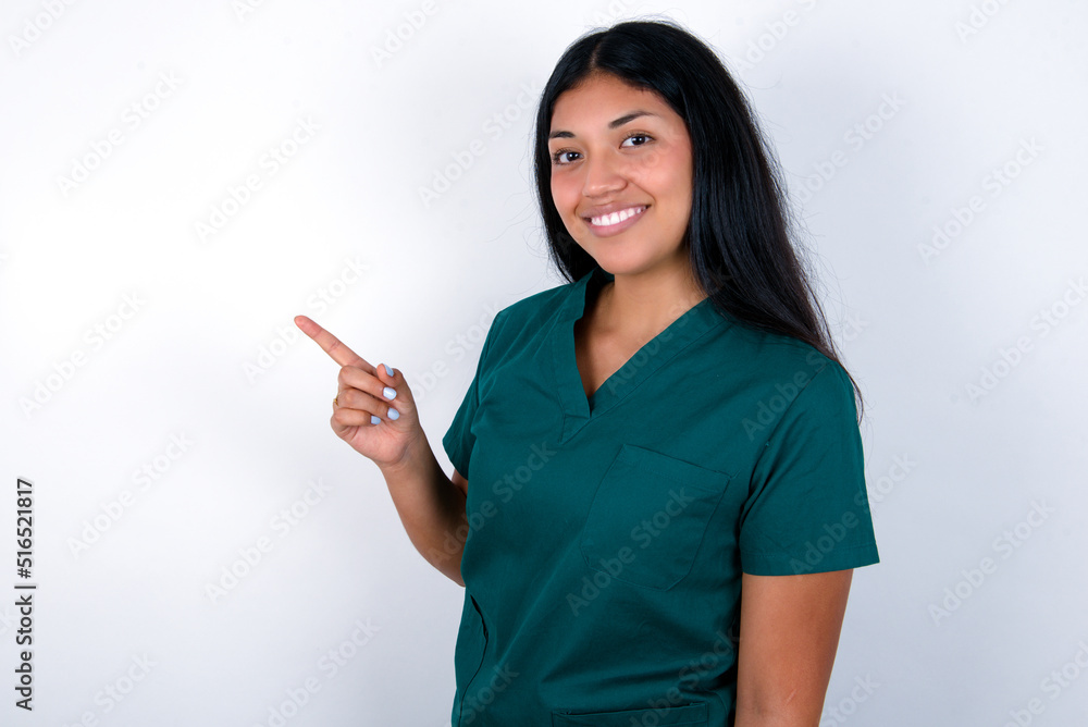 Profile photo of Doctor hispanic woman wearing surgeon uniform over white background indicate finger empty space offer Profile photo of Doctor hispanic woman wearing surgeon uniform over white background indicate finger empty space offer