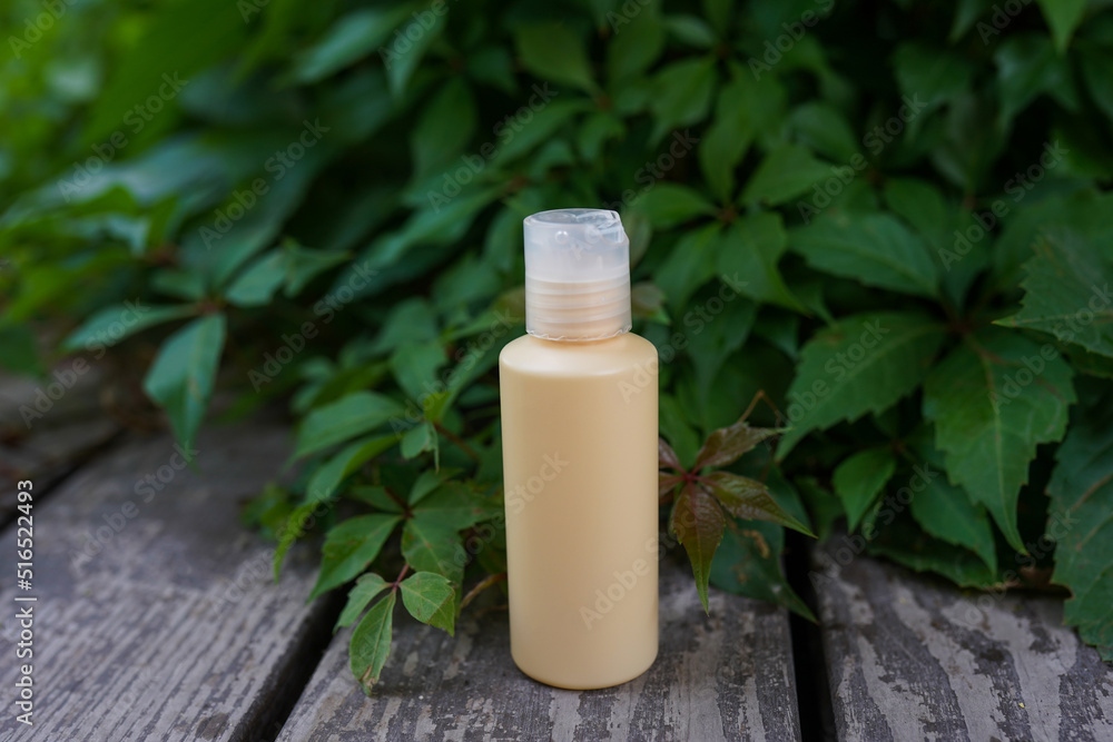 Yellow cosmetic bottle with skin care oil or lotion staying on the wood with green leaves background Yellow cosmetic bottle with skin care oil or lotion staying on the wood with green leaves background