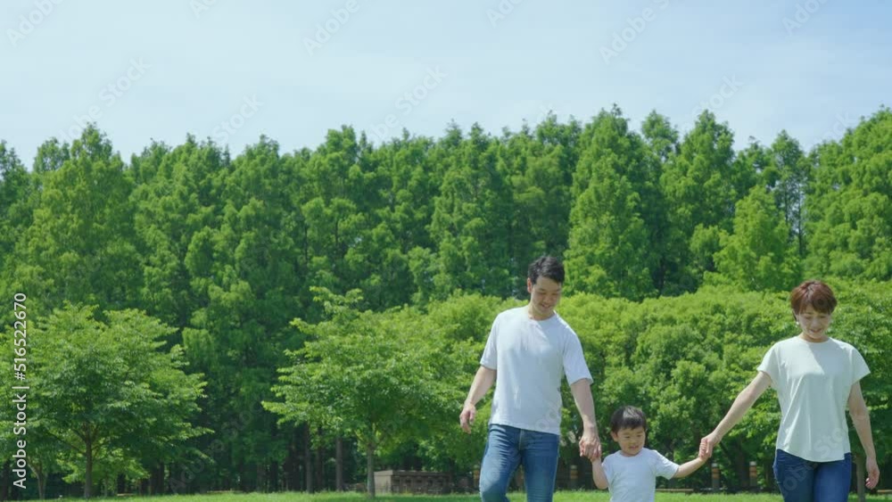 手を繋いで晴天の緑地を歩く親子3人
