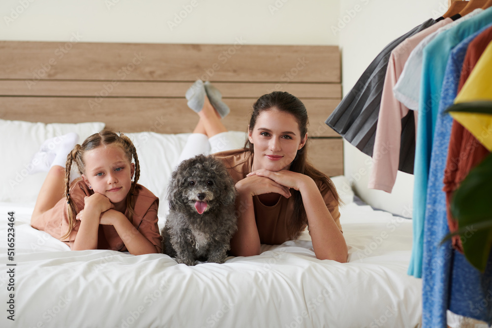 Mother, daughter and little dog lying in bed and smiling at camera Mother, daughter and little dog lying in bed and smiling at camera