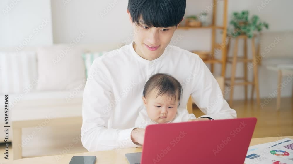 赤ちゃんを抱っこしながら自宅で仕事する男性 赤ちゃんを抱っこしながら自宅で仕事する男性