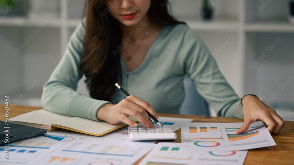 Thoughtful young female investor using calculator and working with statistics document at home office Thoughtful young female investor using calculator and working with statistics document at home office