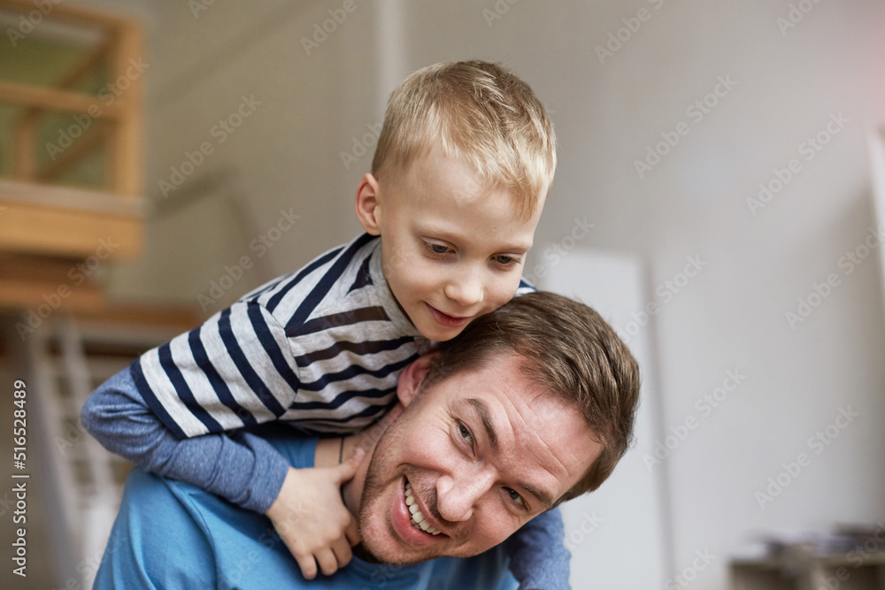 Happy little blond-haired boy climbing fathers neck while they playing active game at home Happy little blond-haired boy climbing fathers neck while they playing active game at home