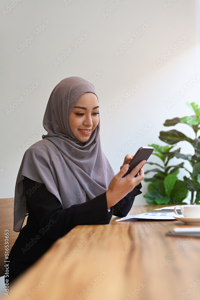 Smiling muslim woman using mobile phone for checking social media or communicating in online community Smiling muslim woman using mobile phone for checking social media or communicating in online community