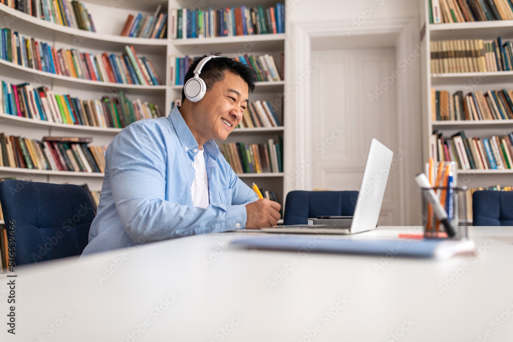 Happy Asian Man Using Laptop And Taking Notes In Library Happy Asian Man Using Laptop And Taking Notes In Library