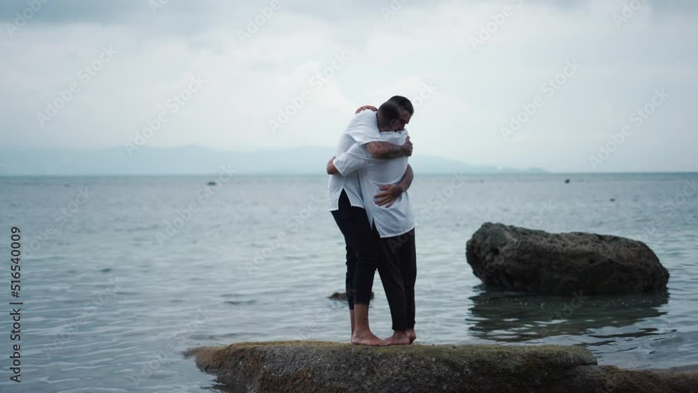 Lovers embrace. An LGBTQ men gay couple holds each other and embraces in a romantic display of love standing on a rock by the sea Lovers embrace. An LGBTQ men gay couple holds each other and embraces in a romantic display of love standing on a rock by the sea