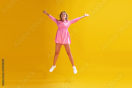 Portrait of beautiful young woman in cute pink dress posing isolated over yellow studio background. Delightful