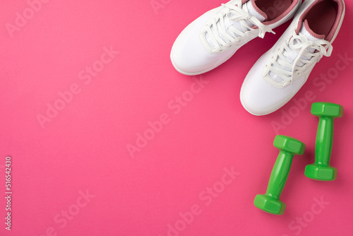 Fitness accessories concept. Top view photo of white sports shoes and green dumbbells on isolated pink background with copyspace