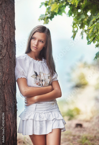 A girl on a summer day walks alone near a cliff on the seashore. She is in white clothes