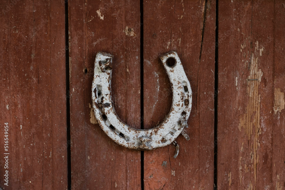 An old horseshoe hangs on old wooden doors.The concept of tradition of different peoples. An old horseshoe hangs on old wooden doors.The concept of tradition of different peoples.