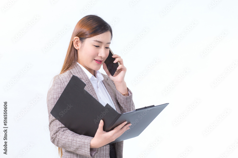 Asian working woman in formal suit with white shirt is calling telephone and opens document file or clipboard to check data. Asian working woman in formal suit with white shirt is calling telephone and opens document file or clipboard to check data.
