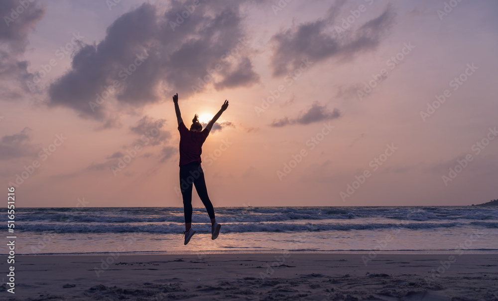 Silhouette of a young woman in sportswear jumping on the seashore at sunset or dawn