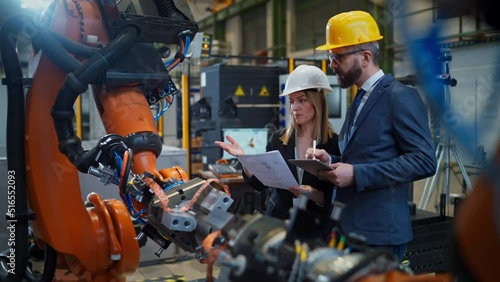 Chief engineer and project manager in modern industrial factory with robot arms talking and planning optimization of production.