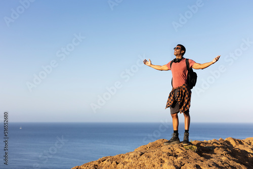 Young man standing on the stone with raised up arms. Tourist man on the top of the mountain...