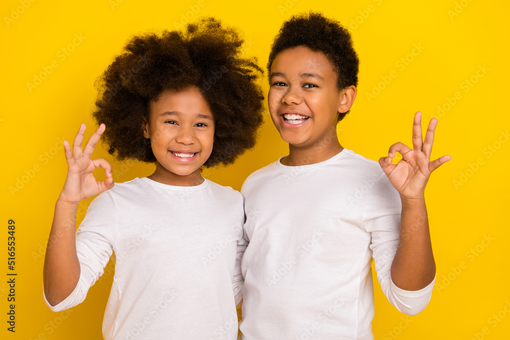 Photo of confident shiny schoolkids dressed white shirts showing two okey signs isolated yellow color background Photo of confident shiny schoolkids dressed white shirts showing two okey signs isolated yellow color background