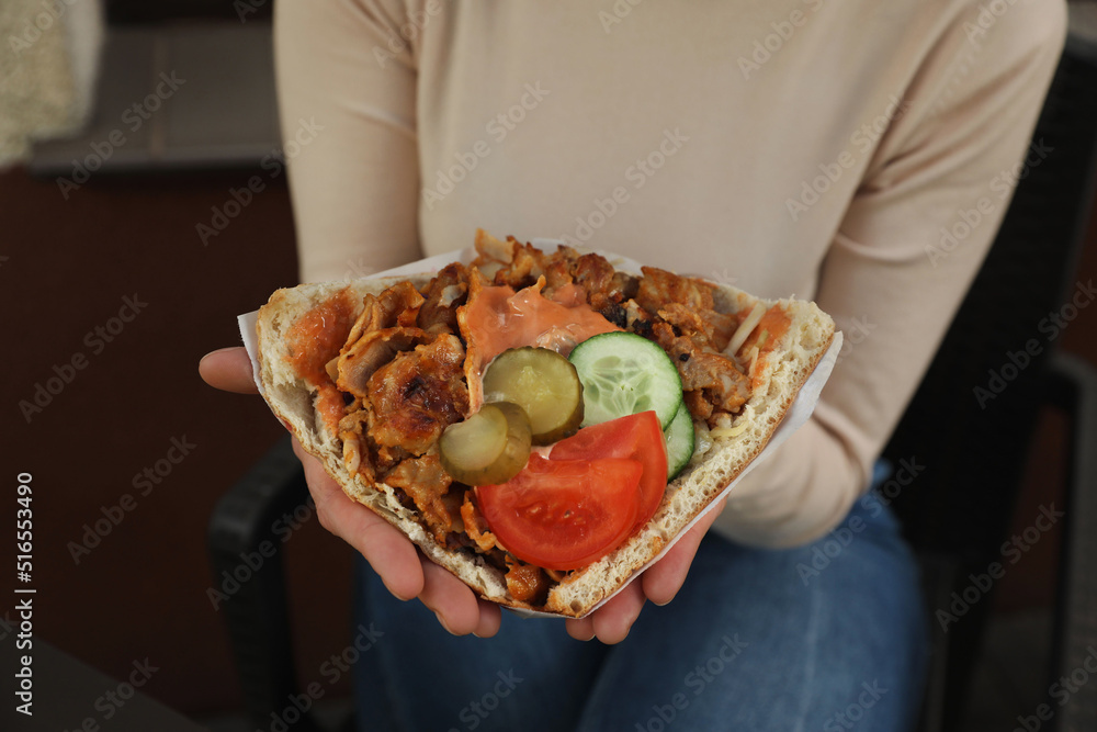 Woman holding delicious bread with roasted meat and vegetables indoors, closeup. Street food
