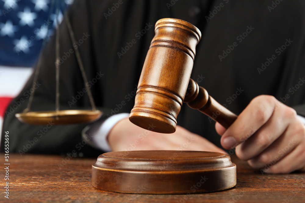 Judge with gavel at wooden table near flag of United States, closeup Judge with gavel at wooden table near flag of United States, closeup