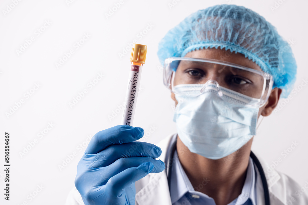 African american male doctor wearing face mask, holding vial with monkeypox virus