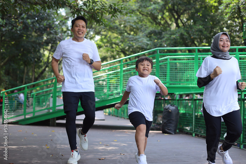 Happy Asian mother, father and little boy running and playing catch game in greeny park. Family, parenthood, leisure and people concept photo