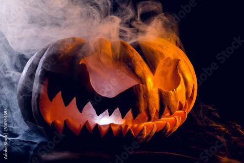 Composition of halloween carved pumpkin with smoke and orange light on black background
