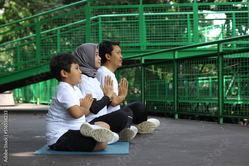  Young Asian family meditating yoga pose together in namaste hands at the greenery park. Healthy lifestyle family concept.