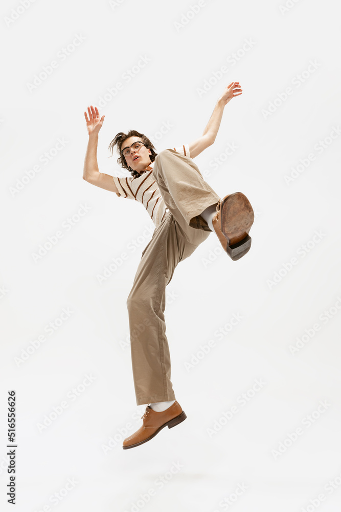 Portrait of expressive young man in vintage outfit dancing, posing isolated over white studio background. Buttom view