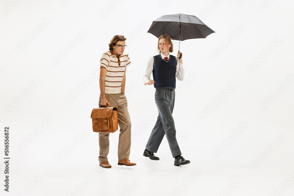 Fototapeta premium Portrait of two seriously looking man in retro style outfit walking isolated over white studio background. Diversity of emotions