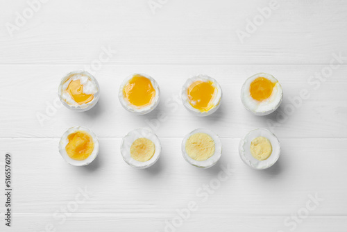Different readiness stages of boiled chicken eggs on white wooden table, flat lay