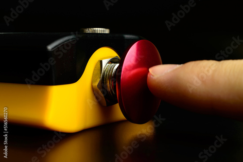 Macro photo of an emergency stop button on a remote controller for ship's crane. A finger is pushing red button. Nuclear weapon - start button. Military danger - risk of war.
