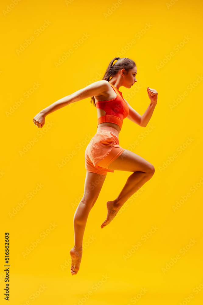 Full-length portrait of young slim girl running isolated on bright yellow background. Modern sport, action, motion, summer, vacation, youth concept. Full-length portrait of young slim girl running isolated on bright yellow background. Modern sport, action, motion, summer, vacation, youth concept.
