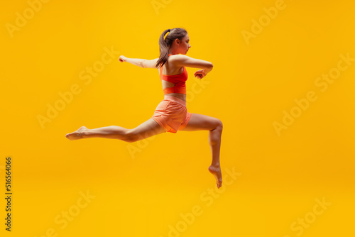 Full-length portrait of young slim girl running isolated on bright yellow background. Modern sport, action, motion, summer, vacation, youth concept.
