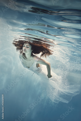 A girl in a white dress with lace swims underwater as if flying