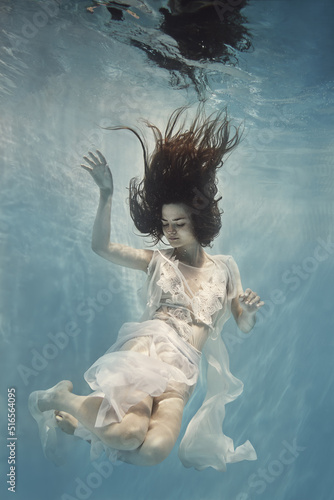 A girl in a white dress with lace swims underwater as if flying