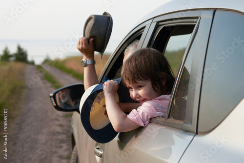 A fragment of a car with a happy child in the window. A motorist and a girl wave straw hats as they approach the seashore. Selective focus. photo