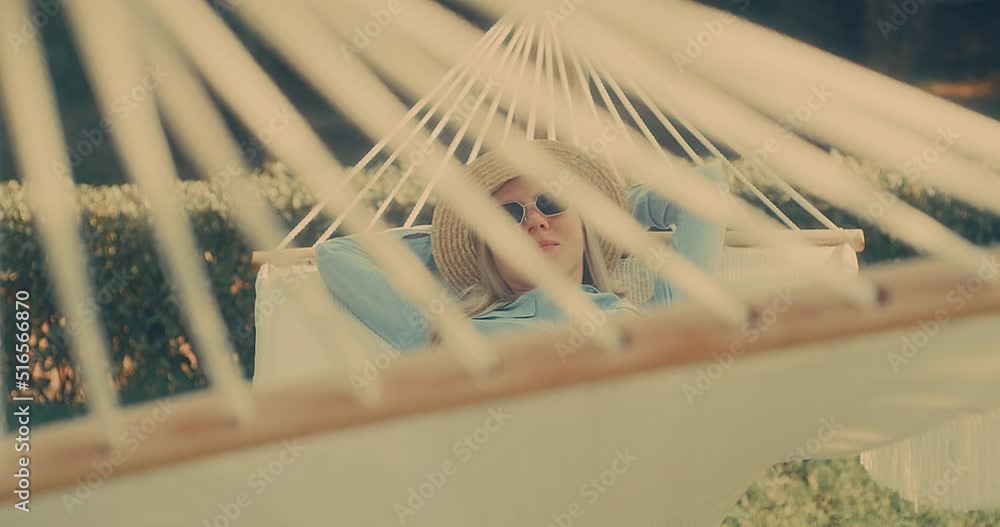 woman in hat and sunglasses is resting in hammock in garden, in sunny summer day. Health care, authenticity, sense of balance and calmness. Spend free time. woman in hat and sunglasses is resting in hammock in garden, in sunny summer day. Health care, authenticity, sense of balance and calmness. Spend free time.