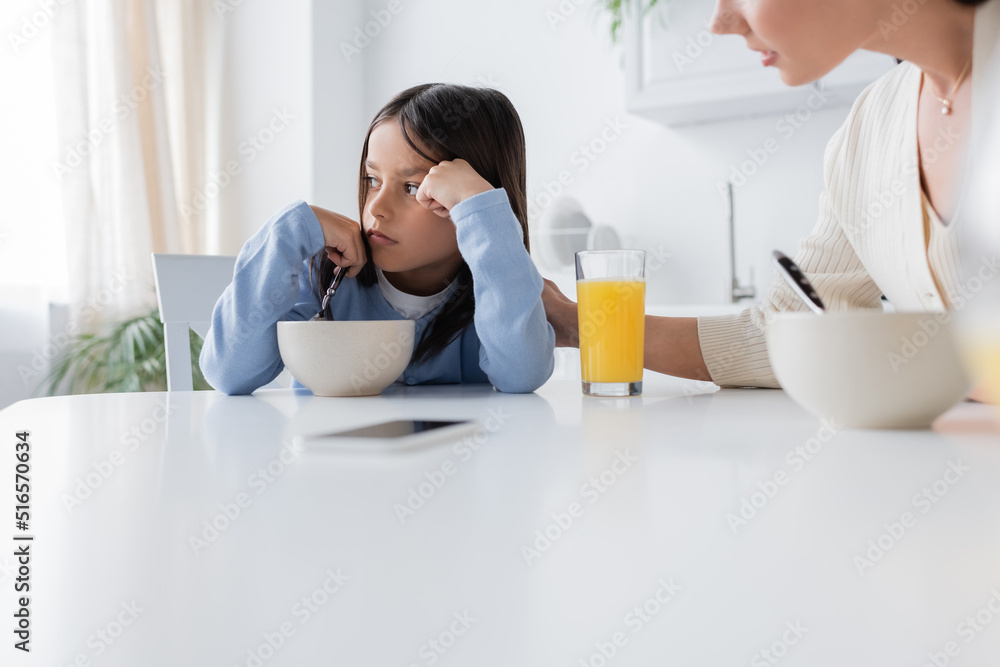 offended girl looking away near breakfast and blurred nanny in kitchen. offended girl looking away near breakfast and blurred nanny in kitchen.