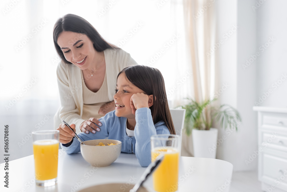 happy babysitter looking at smiling girl having breakfast in kitchen.