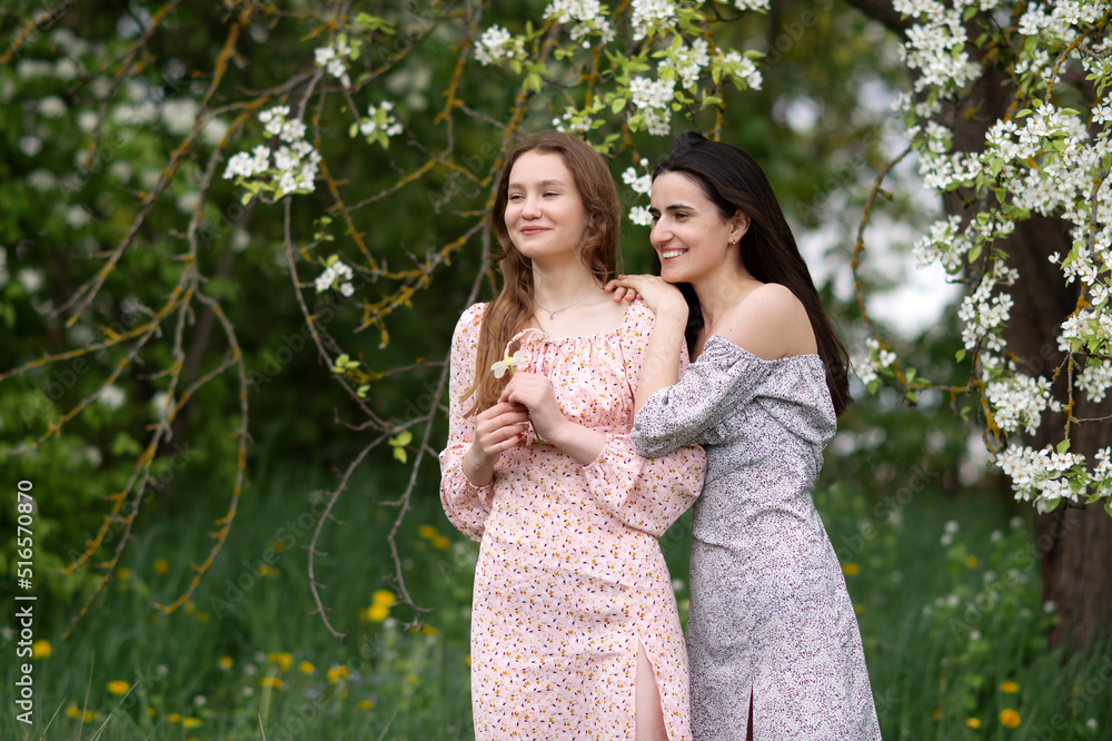 Two young girls in dresses are standing under a white tree laughing and looking away Two young girls in dresses are standing under a white tree laughing and looking away