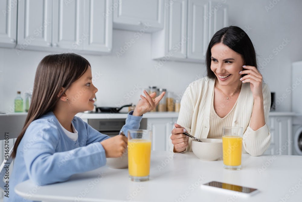 girl talking to happy nanny near bowls with breakfast and fresh orange juice. girl talking to happy nanny near bowls with breakfast and fresh orange juice.
