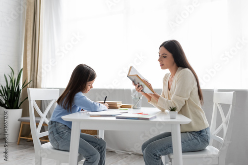 Foto side view of babysitter reading aloud near girl writing dictation at home