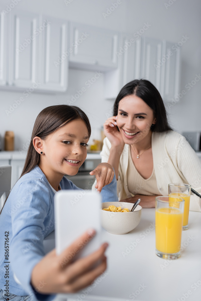 happy girl showing blurred mobile phone to babysitter during breakfast.