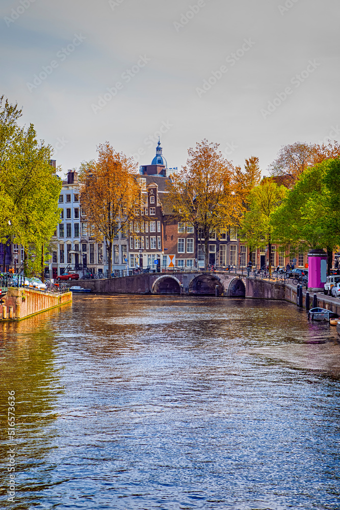 Holland Travel Destinations. Romantic Amsterdam River Canal with Boat Cruises For Guests and Visitors Along Shores with Arched Bridges in Amsterdam.