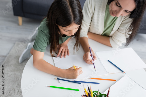 high angle view of brunette babysitter and kid drawing on paper.