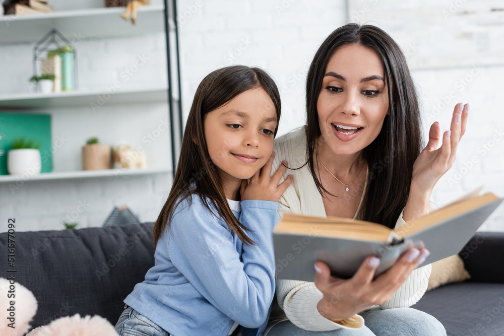 babysitter reading book to smiling girl and gesturing on blurred foreground. babysitter reading book to smiling girl and gesturing on blurred foreground.